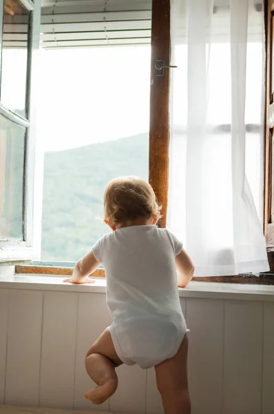 Mutlu sarışın bebek oynarken yatakta oturan ve evde pencereye bakarak