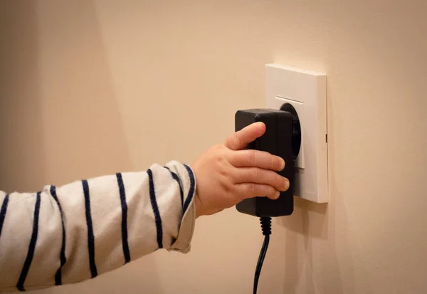 Küçük bir çocuğun eli elektrik prizi ve trafo ile oynuyor. Yakın çekim.