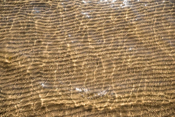 Sand background texture under water. Transparent water ripple, sand waves and sunlight glare. Sea bottom background