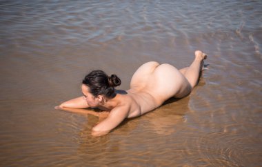 Denizde poz veren güzel çıplak genç bir kadın. Çıplakken seksi Yazın sahilde eğleniyor