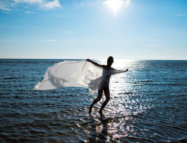 Young naked woman wrapped in white shawl posing at the beach.  Enjoying summer time outdoors clipart