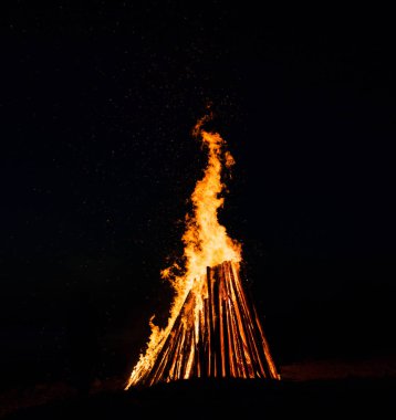 Karanlık gökyüzüne karşı büyük şenlik ateşi. Siyah arkaplanda yangın alevleri