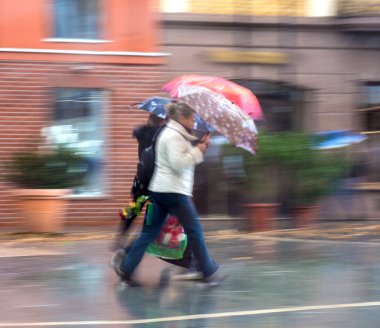 Yağmurlu günde sokakta yürürken şemsiye insanlarla. Kasıtlı hareket bulanıklığı. Ufuk yansıma