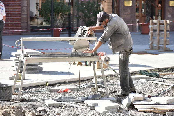 Worker cutting granite tiles with an diamond electric saw blade at a construction site