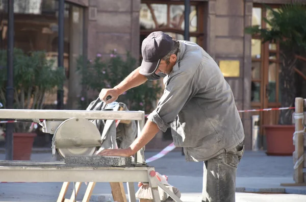 Worker cutting granite tiles with an diamond electric saw blade at a construction site