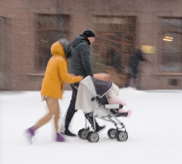 家族は 雪に覆われた冬の日にベビーカーで子供と歩きます 意図的なモーションブラー イメージ — ストック写真