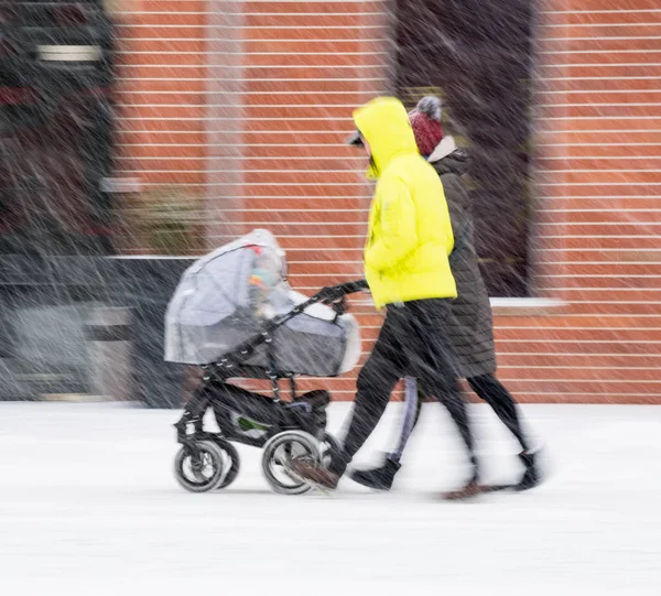 家族は 雪に覆われた冬の日にベビーカーで子供と歩きます 意図的なモーションブラー イメージ — ストック写真