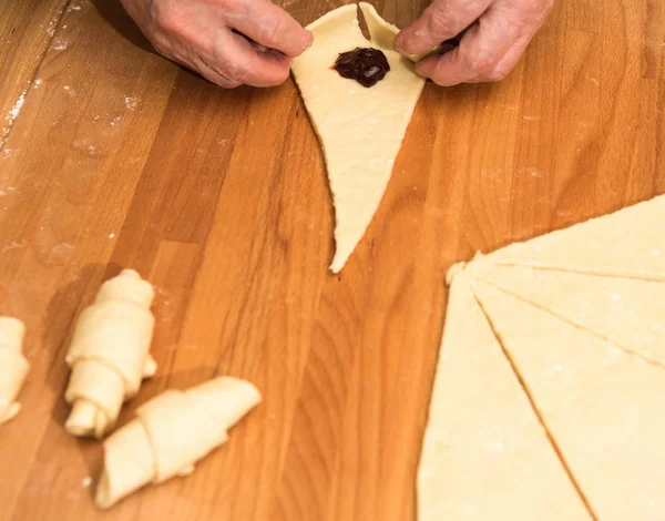 Producing classic croissants at the bakery shop. Woman is rolling dough into rolls for further baking