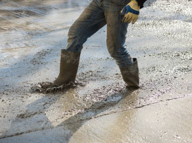 İşçi inşaat yerinde taze dökülmüş beton veya çimento üzerinde çalışıyor. Yeni kentsel yol sokak projesi 
