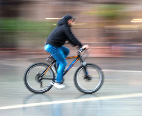 Ciclista en la carretera de la ciudad en movimiento borrosa en días lluviosos. Intenti — Foto de Stock