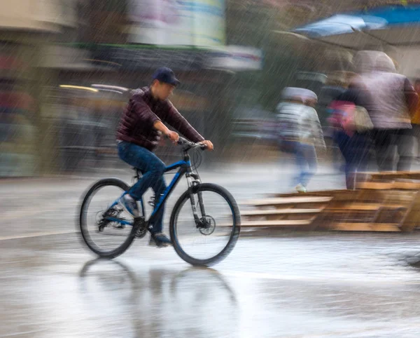 Велосипедист на проїжджій частині міста розмивається в дощовий день. Інтенті — стокове фото
