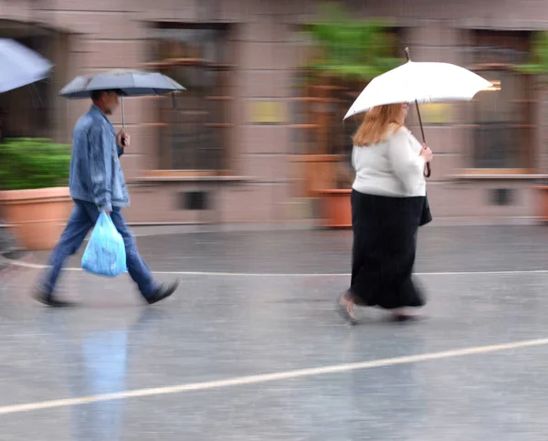 Menschen mit Regenschirm laufen bei Regen die Straße hinunter — Stockfoto