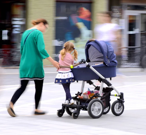 Bebek arabasında küçük çocuklu genç anne s aşağı yürüyor — Stok fotoğraf