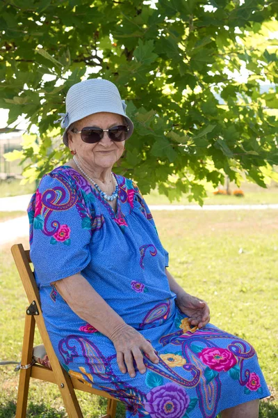 Velha mulher sorridente em sungalsses sentado em uma cadeira — Fotografia de Stock