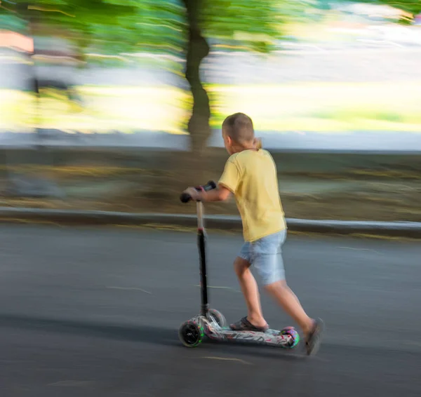 Liten pojke ridning skoter utomhus. Gatustads bakgrund — Stockfoto