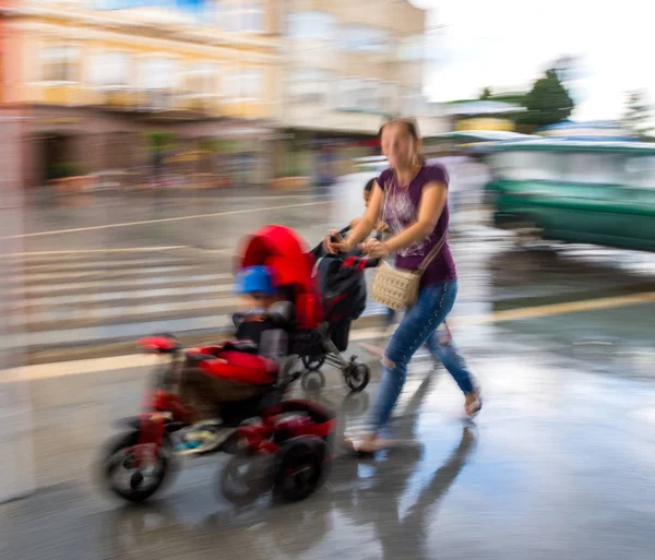 ベビーカーに小さな子供を持つ若い母親が歩いて — ストック写真