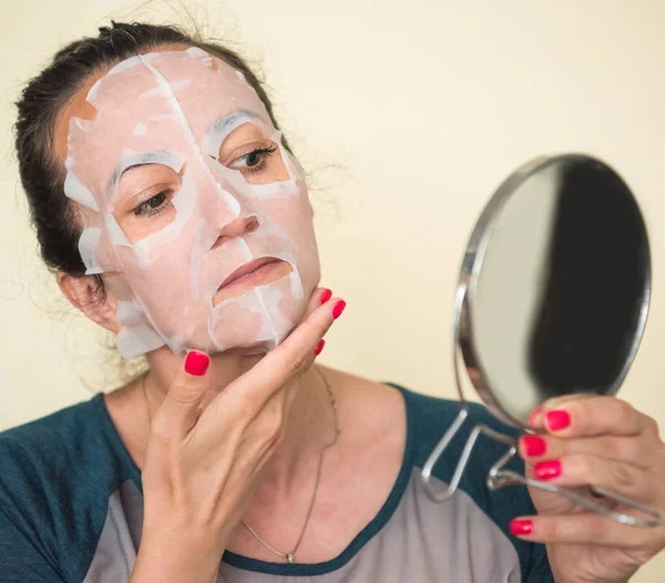 Женщина наносит маску из косметической ткани на лицо дома — стоковое фото