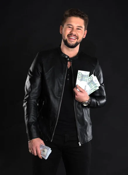 Молодой красивый мужчина в черной кожаной куртке держит долларовые купюры — стоковое фото
