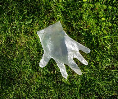 Bir koronavirüs salgını sırasında tek kullanımlık plastik eldiven çimenlerin üzerinde uçar.