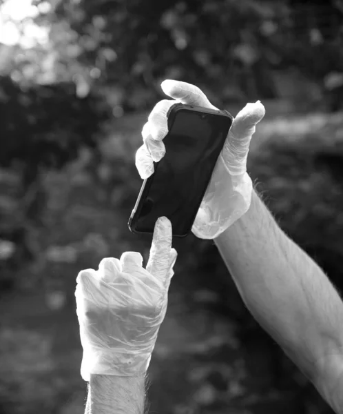 Man in disposable gloves holding smartphone outdoors