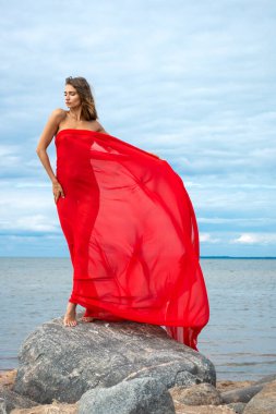 Deniz sahilinde poz veren kırmızı şallı güzel çıplak kadın. Açık havada seksi esmer