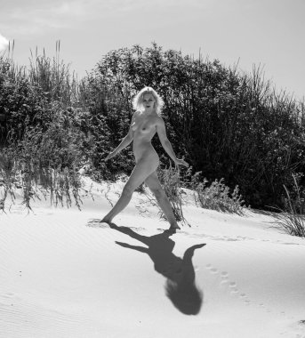 Kumsalda poz veren çıplak bir kadın. Seksi sarışın, sıcak yaz gününün tadını çıkarıyor.
