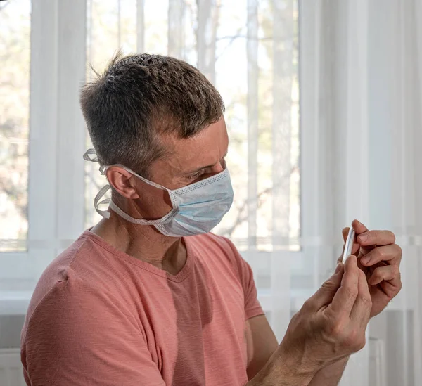 Opieka Zdrowotna Koncepcja Medyczna Mężczyzna Masce Ochronnej Trzyma Termometr Domu — Zdjęcie stockowe