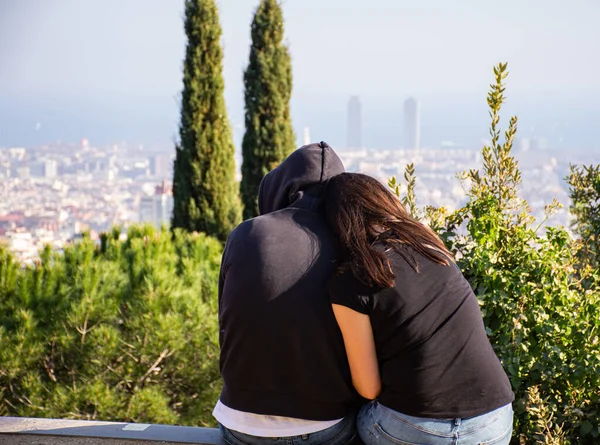 Back view of beautiful young couple hugging while sitting and resting in the park