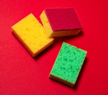 Kırmızı arka planda bulaşık yıkamak için çok renkli süngerler.