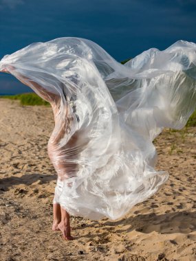 Genç çıplak kadın sahilde polietilen filmde poz veriyor.