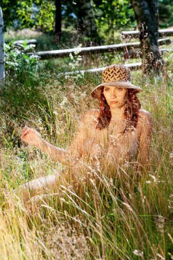 Çimlerde çıplak bir kadın, güneş ışığında doğal arka planda.