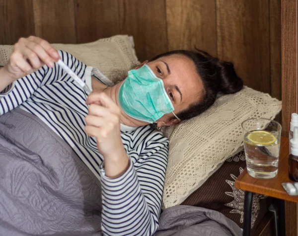 医療と医療の概念 インフルエンザウイルスを持つ女性は 自宅で温度計で温度を測定し ベッドに横たわっている — ストック写真