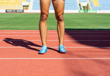 Spor yaşam tarzı. Spor ayakkabılı kaslı bacaklar güneşli bir günde stadyumda duruyor.