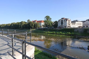 Uzhhorod, Ukraine -  August 11, 2025: Riverside view with reflections of trees and buildings in warm afternoon light in a quaint town in Uzhhorod