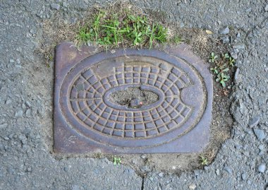 Geometrik desenli dekoratif rögar kapağı çatlak bir asfalt yüzeyde yer almaktadır.