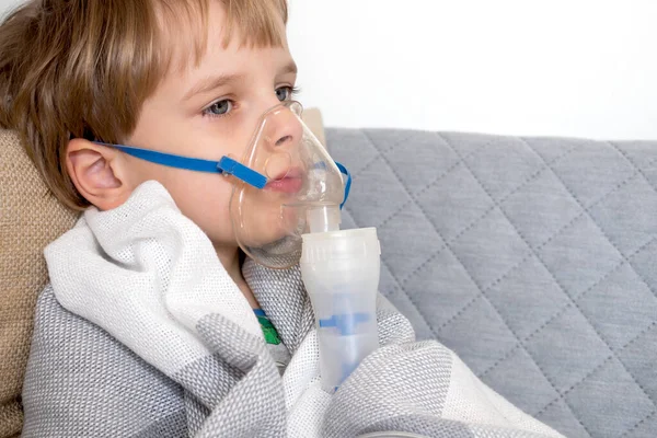 Menino caucasiano a fazer inalação com nebulizador em casa. Criança segura um inalador de vapor máscara. Tratamento da asma. Conceito de aparelho de terapia inalatória . — Fotografia de Stock