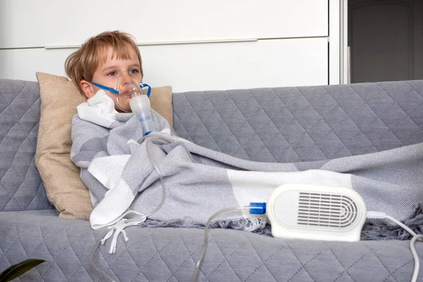 Little caucasian boy making inhalation with nebulizer at home. Child holds a mask vapor inhaler. Treatment of asthma. Concept of inhalation therapy apparatus.