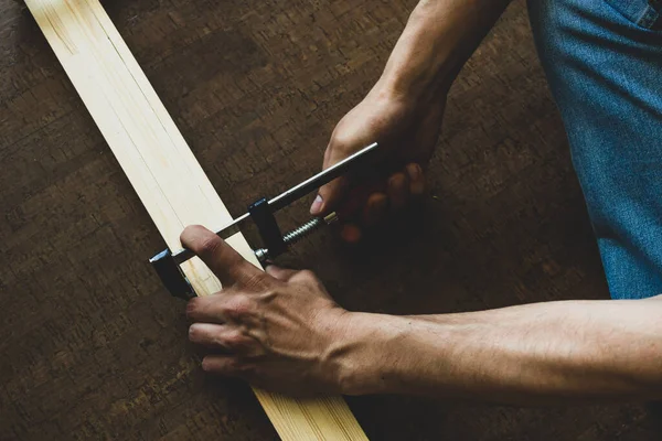 Mens χέρια στερεώστε το σφιγκτήρα στις ξύλινες ράγες, κάνοντας μια μέτρηση πριν από την κοπή. Έννοια επισκευής — Φωτογραφία Αρχείου