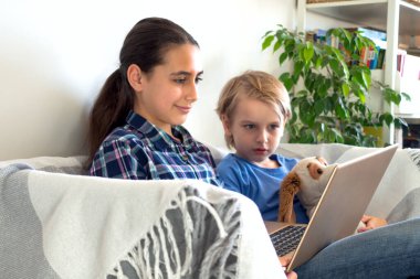 Çevrimiçi eğitim ve çalışma mesafesi. Evden uzakta çocuk eğitimi kanepede oturuyor. Taşınabilir laptop kullanılıyor