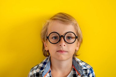 Sarı arka planda beyaz tişörtlü sevimli ve zeki sarışın çocuk portresi. 1 Eylül. Eğitim ve okul konseptine geri dönüş. Öğrenmeye ve çalışmaya hazır çocuk öğrenci.
