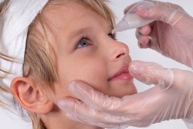 Kadın eli optometrist şeffaf tıbbi eldiven takıyor göz damlası gibi küçük sarışın çocuk gözlerini göz doktoru kliniğine koyuyor. İğrenç bir bakış. Beyaz arkaplan.