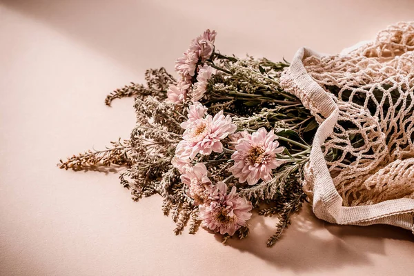Mooi boeket van roze chrysant bloemen in een mesh zak op lichtroze beige achtergrond. — Stockfoto
