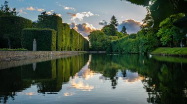 High hedge, clouds and its reflection in the pond at the Oliwa Park clipart