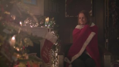 Güzel kız Noel ağacın yanında oturup rahat bir battaniyeye sarılmış