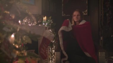 Güzel kız Noel ağacın yanında oturup rahat bir battaniyeye sarılmış