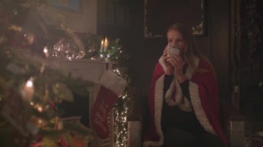 Güzel kız Noel ağacın yanında oturan ve sıcak çikolata içme rahat bir battaniyeye sarılmış