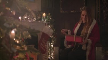Sevimli kız oturma Noel ağacının yanındaki ve bir hediye açılırken mutlu görünüyordu