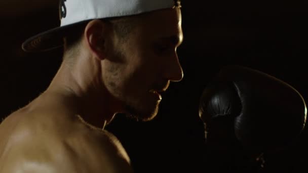 Jovem durante o treinamento de boxe no fundo escuro batendo o saco de perfuração nas luvas de boxe tiro na câmera vermelha — Vídeo de Stock