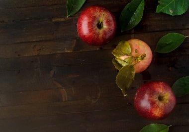 Bir sarı pembe apple ve ahşap arka plan yapraklarda ile iki kırmızı elma.