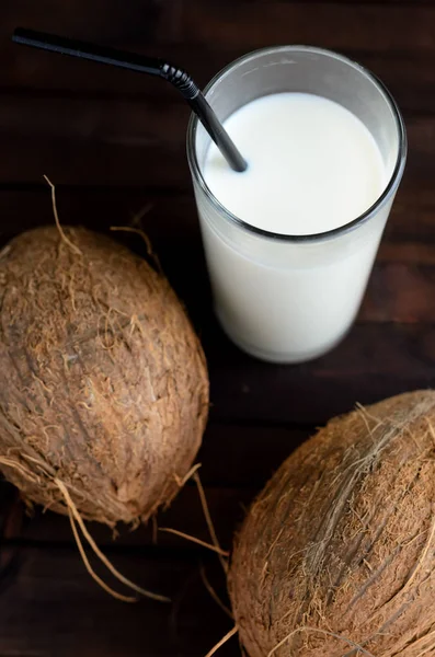 A glass of coconut milk and two whole coconuts.